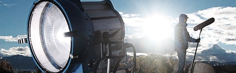 Stor filmlyskaster og person i silhuett mot en lys himmel